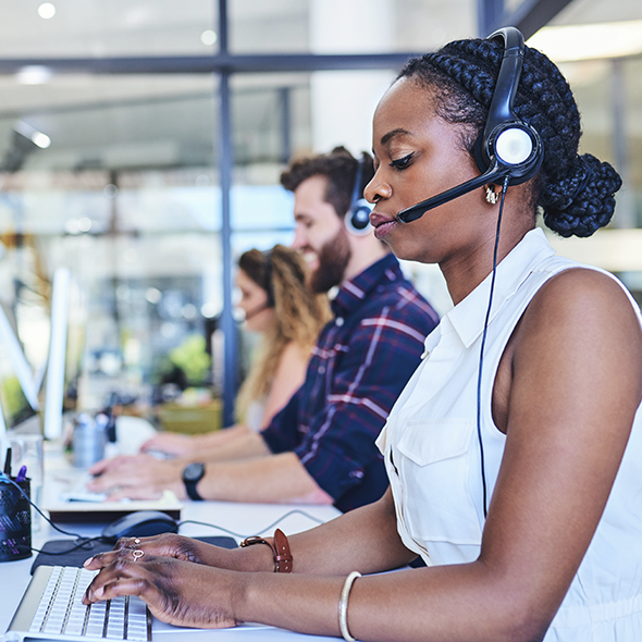Women and man with headsets at desktops in a call center using AppDynamics in Cisco Unified Contact Center Enterprise (UCCE)