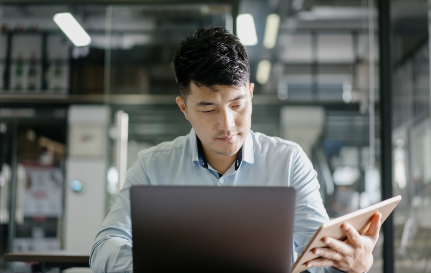 Man at desk with a laptop and a tablet improving his company's security posture via Runtime Application Self-Protection